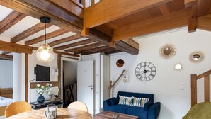 Een gezellige kamer met een houten plafond, een blauwe bank, een eettafel met stoelen en een wandklok.