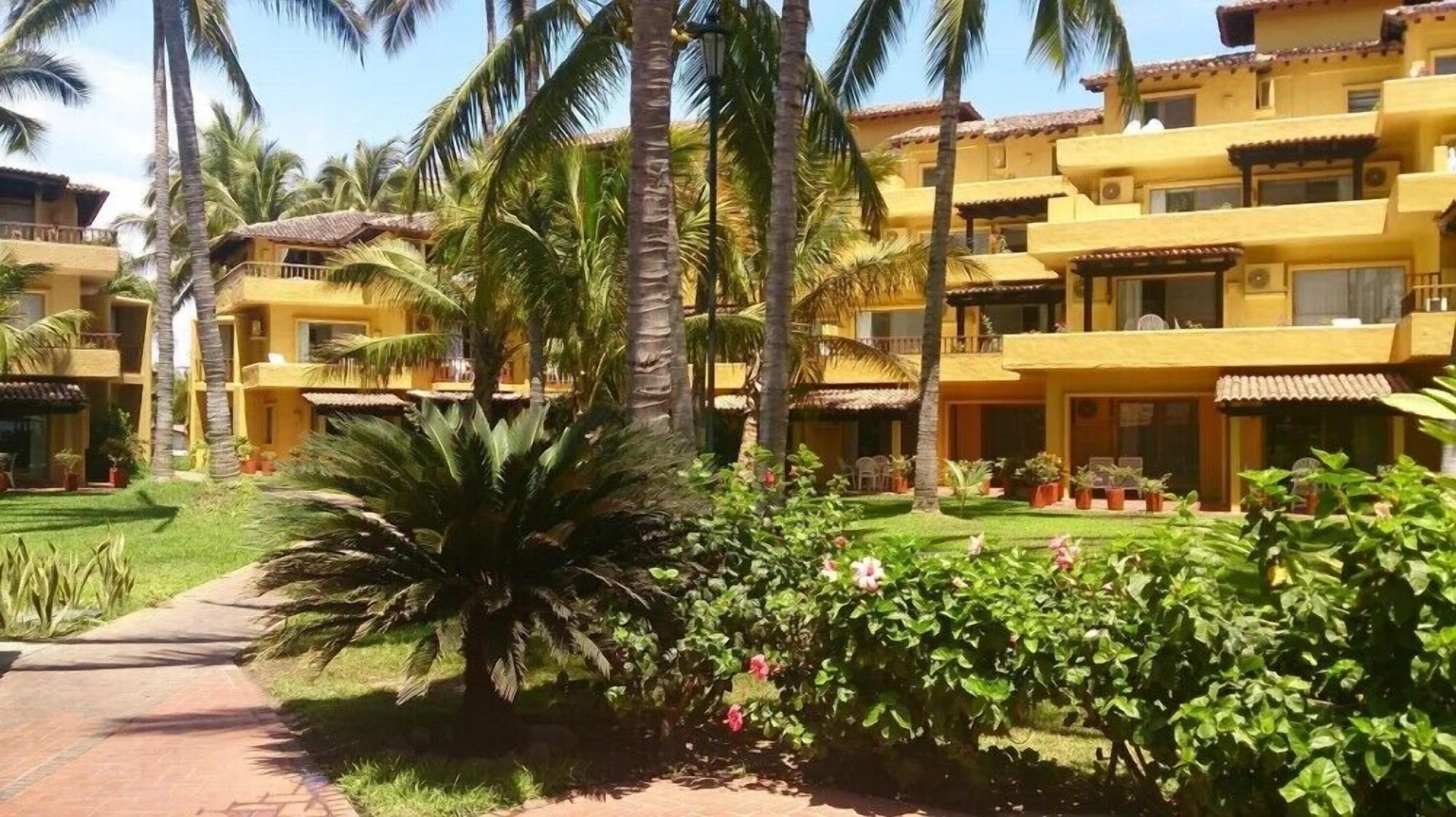 A resort with multiple yellow buildings, palm trees, and a well-maintained garden with a pathway.