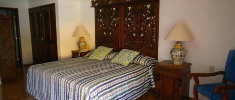 A bedroom with a large bed, two bedside tables with lamps, a wooden headboard, and a blue chair.