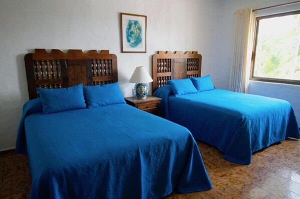 Une chambre avec deux lits, une table de chevet avec une lampe, un tableau encadré au mur et une fenêtre avec des rideaux.