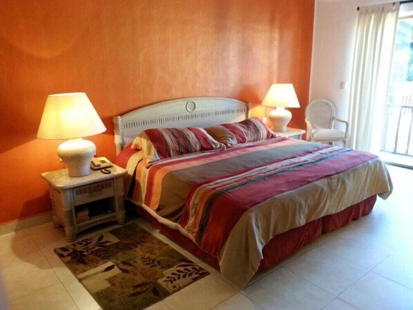 Un dormitorio con una cama, dos mesitas de noche con lámparas, una silla y una alfombra estampada.