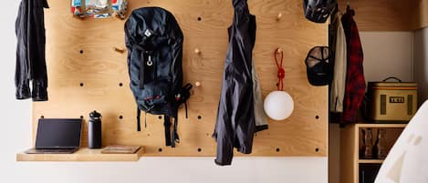 A room with a wooden pegboard wall displaying various items such as a laptop, a backpack, and a helmet.