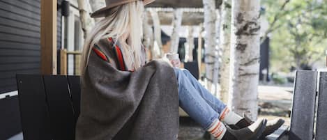 A person sitting on a bench outdoors, wrapped in a blanket, holding a cup.