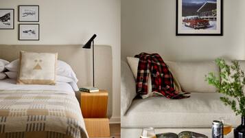 A hotel room with a bed, a sofa, a coffee table with a book, a glass of beer, and a can of beer.