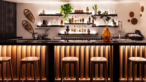 Un espace bar moderne avec des tabourets en bois, des étagères remplies de bouteilles et des objets décoratifs.