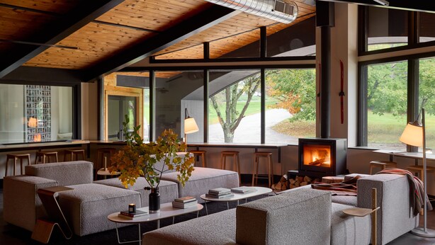 Un intérieur moderne avec une cheminée, un coin salon et de grandes fenêtres donnant sur l’extérieur.