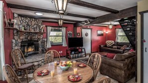A dining area with a stone fireplace, wooden chairs, a round table with plates and glasses, and a red wall. - Pet-Friendly [no fee!] A-Frame Cabin w/ Double-decker Mountain View & Hot Tub (Alto)