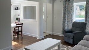 A living room with a grey sofa, a white coffee table, and a patterned rug. There is a dining area with a white table and chairs, and a kitchen area with a white cabinet and a plant. - Gorgeous Ranch Home in Beautiful Westlake Ohio- No Cleaning Fee! (Westlake)