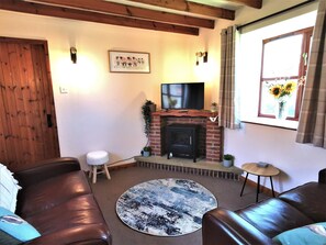 Ein gemütliches Wohnzimmer mit Kamin, Ledersofas, einem runden Teppich und einem über dem Kamin montierten Fernseher.