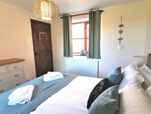 Ein Schlafzimmer mit Bett, Nachttisch, Schminktisch, Fenster mit Vorhängen, Heizkörper und Wanddekorationen.
