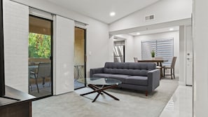 A modern living room with a grey sofa, a glass coffee table, and a dining area with a table and chairs.