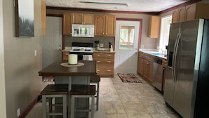 Una cocina con armarios de madera, un refrigerador de acero inoxidable y un comedor con mesa y sillas.