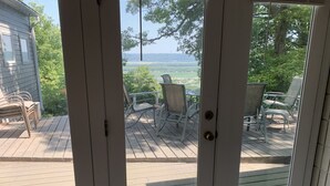 A view through a glass door to an outdoor patio with a table and chairs, overlooking a green landscape. - Sunrise on Skyline - Indoor spa - Arcades - Amazing Views! (Wabasha)