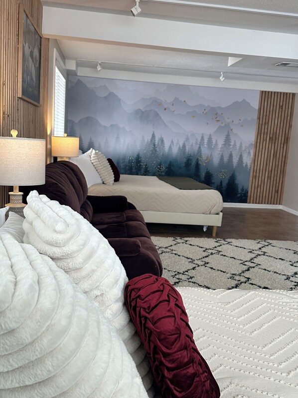 A modern bedroom with a large bed, a sofa, and a mural of a forest. - Sunrise on Skyline - Indoor spa - Arcades - Amazing Views! (Wabasha)