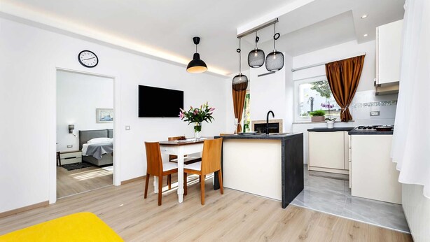 Une cuisine moderne avec un coin repas, un téléviseur fixé au mur et une horloge au mur.