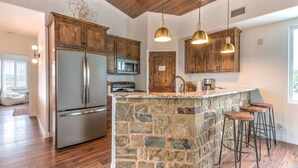 A kitchen with a stone island, stainless steel appliances, wooden cabinets, and pendant lighting. - Getaway Ranch - Views for Days +  Pool + Game Room (Spicewood)