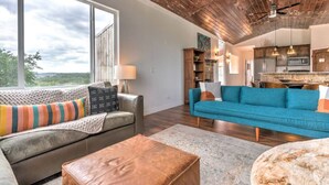 A spacious living area with a sofa, ottoman, and a view of the outdoors. - Getaway Ranch - Views for Days +  Pool + Game Room (Spicewood)
