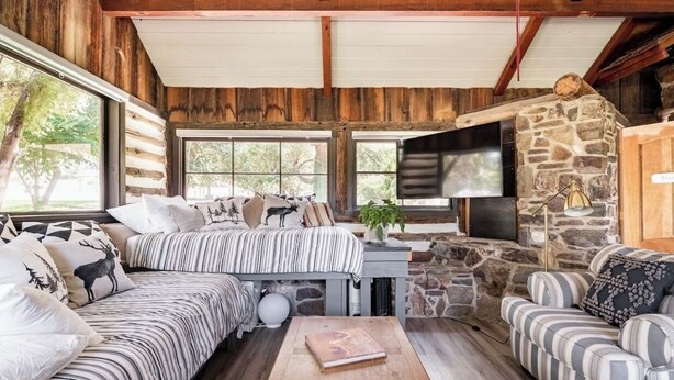 A log cabin interior with a sofa, armchair, and a stone fireplace. - Meadowlands Cottage, Horse Ranch with Wood Burning Stove and a River, Hot Tub (kernville)