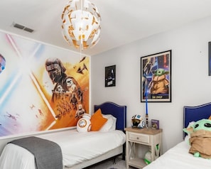 A bedroom with a Star Wars-themed wall mural, a bed with a blue headboard, a bedside table with a Star Wars helmet, and a poster of Baby Yoda.