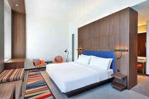 Una habitación de hotel moderna con una cama grande, un pequeño rincón de descanso y un baño visible a través de una puerta abierta.
