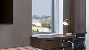 Ein modernes Zimmer mit Schreibtisch, Stuhl, Lampe und Blick auf die Stadt durch ein großes Fenster.