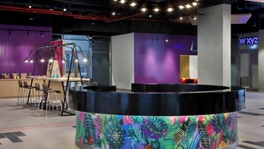 A modern reception area with a circular black counter, colorful tropical wallpaper, and a purple and white wall. - Aloft by Marriott Dubai Airport (Dubai)