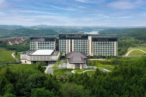 Un hotel Sheraton con diseño moderno, rodeado de vegetación exuberante y una vista panorámica de colinas distantes.