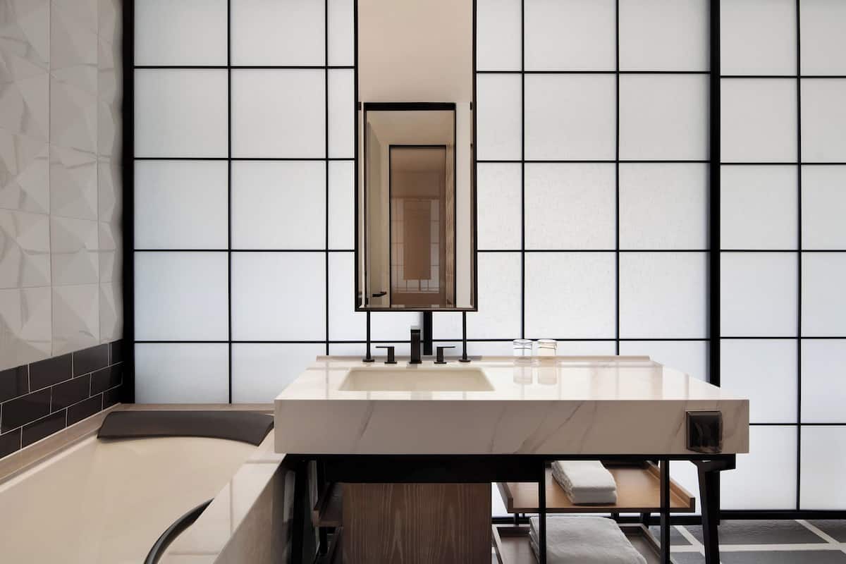 A modern bathroom with a large mirror, a sink, and a bathtub.