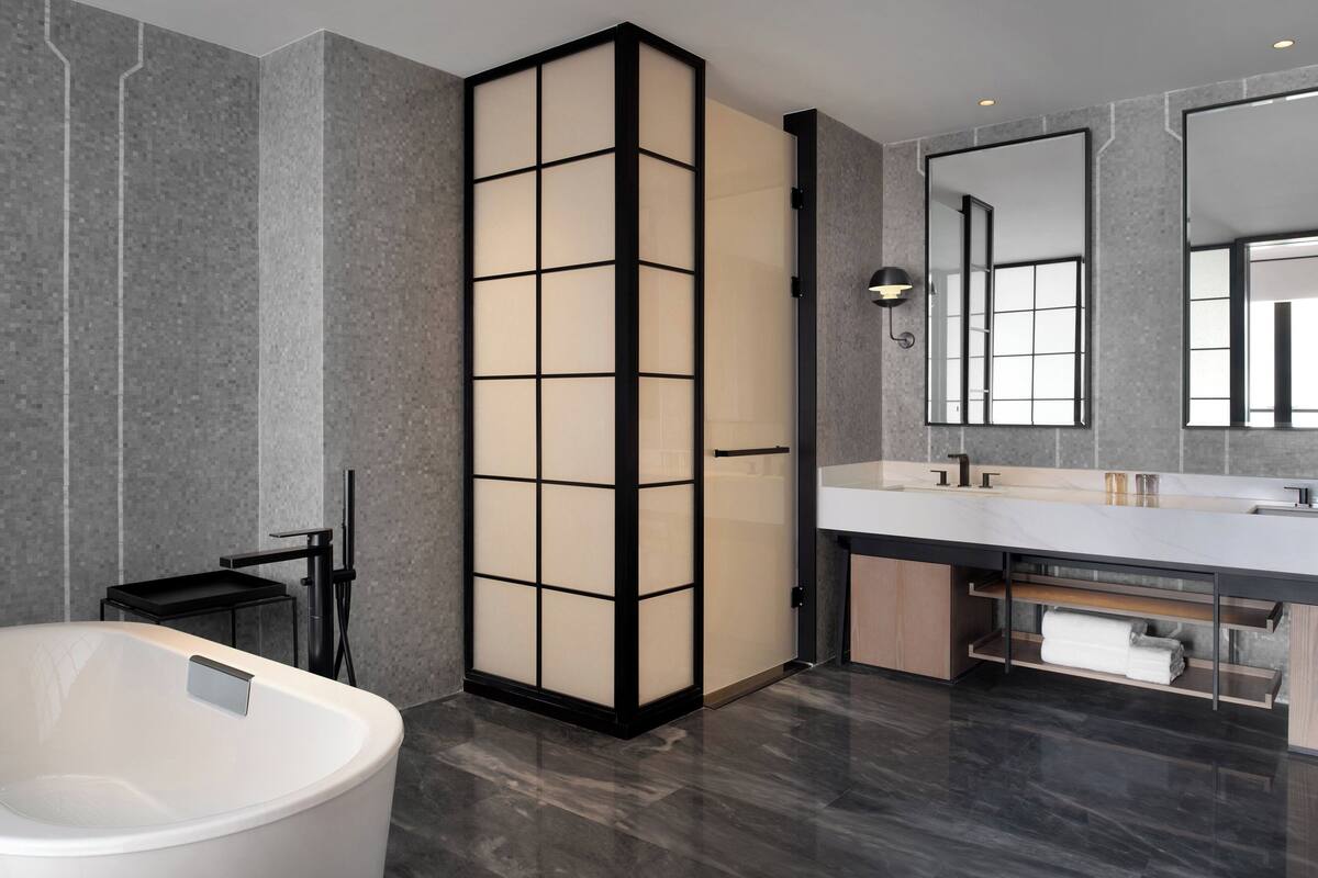 A modern bathroom with a large bathtub, a tall shoji screen, a vanity with a mirror, and a towel rack.