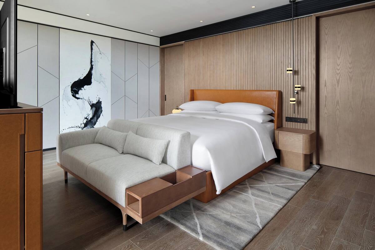 A modern bedroom with a bed, a sofa, and a wooden nightstand.