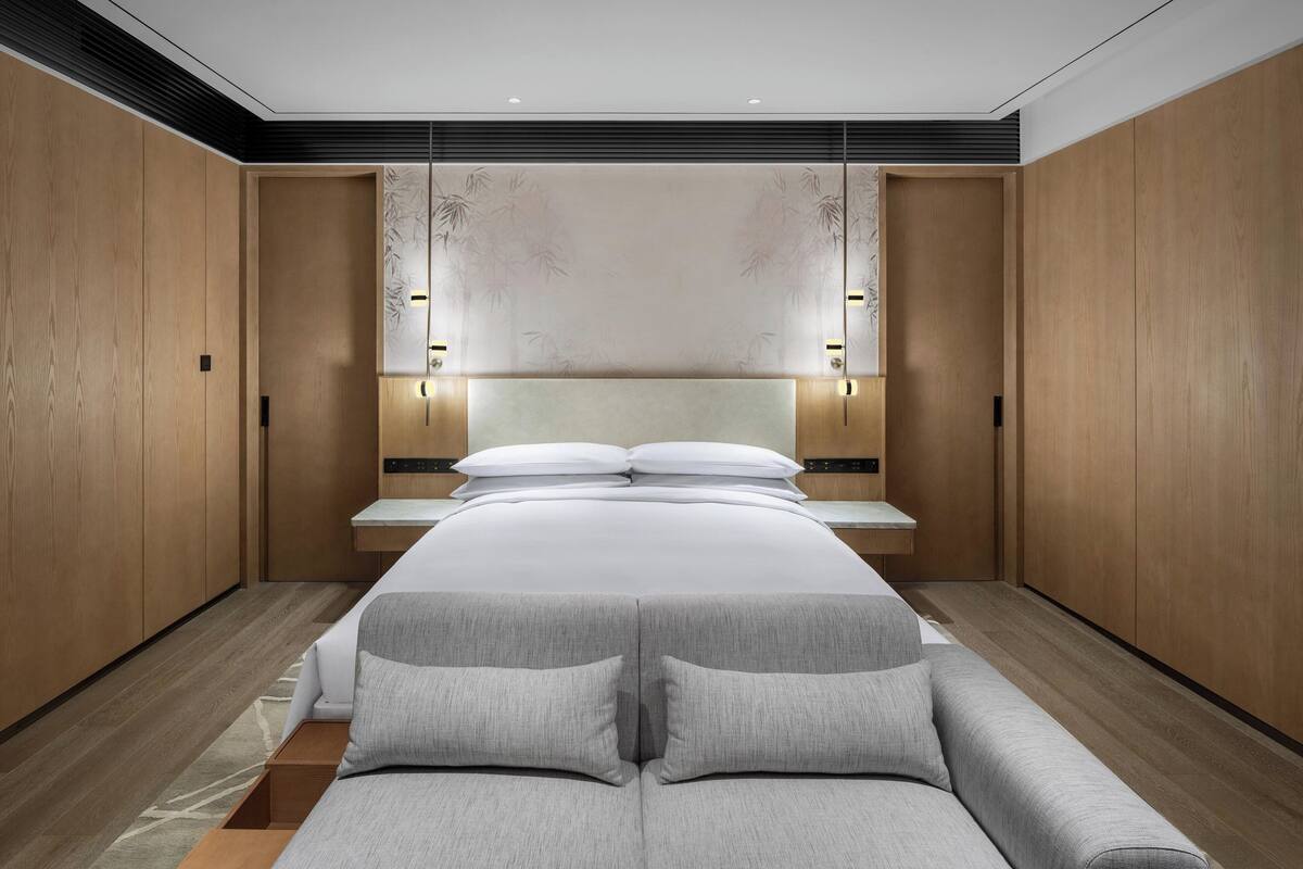 A modern bedroom with a large bed, wooden wardrobe, and a decorative wall panel.