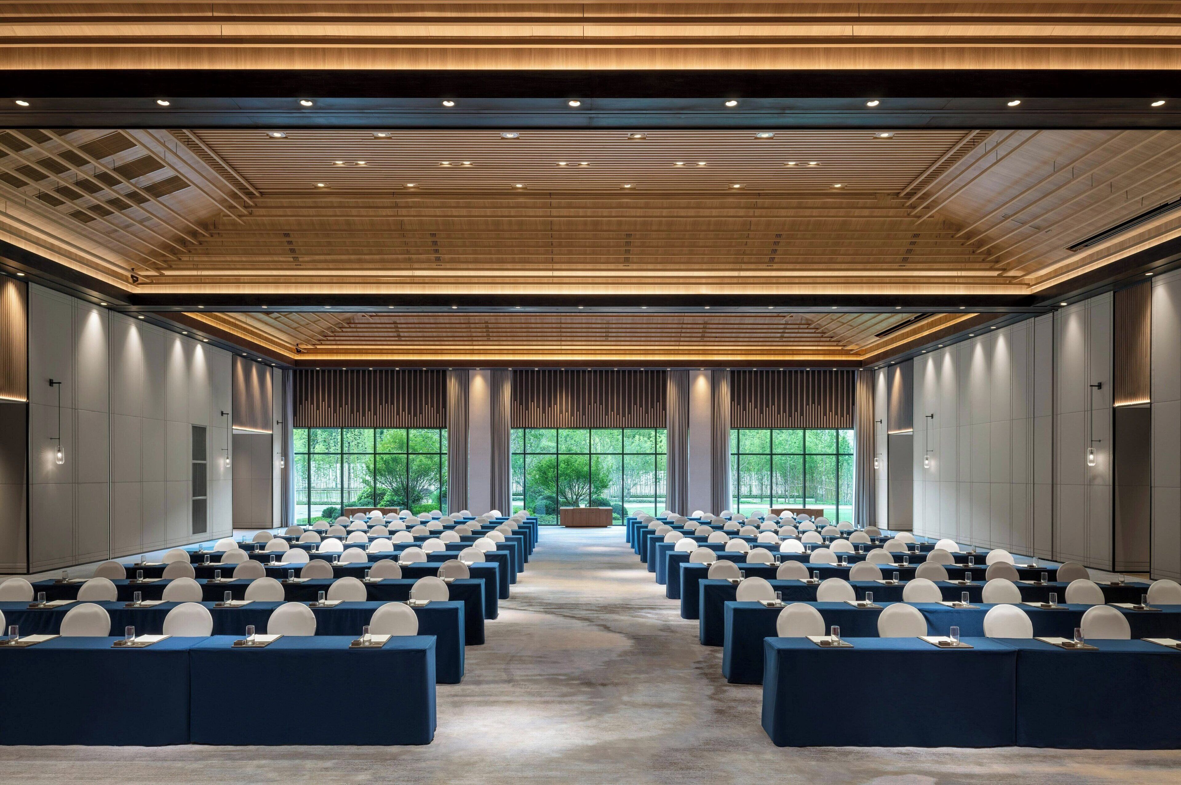A conference room with rows of tables and chairs, large windows, and a wooden ceiling.