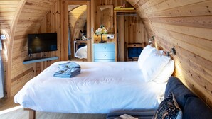 A cozy wooden cabin bedroom with a bed, a sofa, a TV, and a small kitchenette. - Eco Indigo (Dunbar)