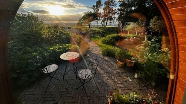 A circular view of a garden with a brick pathway, metal chairs, and potted plants. - Eco Indigo (Dunbar)