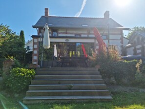 A building with a brick facade, a set of outdoor stairs leading to a patio area with a table and chairs, and a large window.