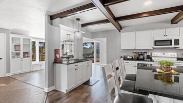 A modern kitchen with white cabinetry, a central island, and a dining area with chairs.