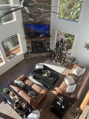 A spacious living room with a stone fireplace, leather sofas, a large flat-screen TV, and a decorated Christmas tree.