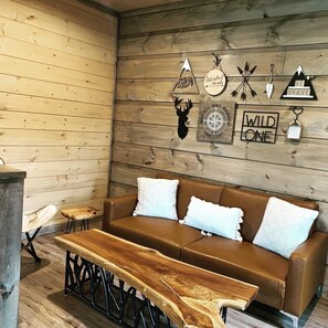 A cozy cabin interior with a wooden wall, a brown leather sofa, and a wooden bench.