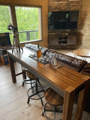 Ein gemütliches Wohnzimmer mit Esstisch aus Holz, Ledersofa und Kamin aus Stein.