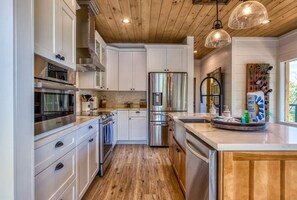 A modern kitchen with stainless steel appliances, wooden flooring, and pendant lighting.