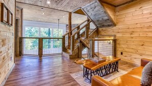 A spacious room with wooden floors, a staircase, and a large window offering a view of greenery.