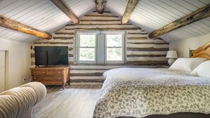 A log cabin bedroom with a wooden bed, a television on a dresser, and a window with a view of greenery. - Mountain View: Hot tub and sauna, next to the river and horses (Kernville)
