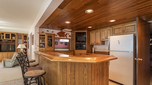 Eine Küche mit Holzschränken, einem Edelstahlkühlschrank und einer Bar mit Hockern.