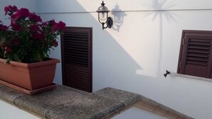 A balcony with a potted plant, a wall-mounted light fixture, and a window with shutters. - Casa vacanze Villa Rosy (nardò)