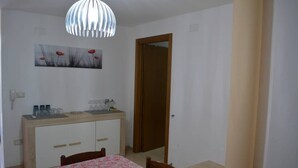 A small, clean room with a wooden cabinet, a table with a floral tablecloth, a hanging light fixture, and a door. - Casa vacanze Villa Rosy (nardò)