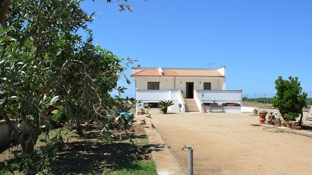 A two-story white building with a tiled roof, a paved driveway, and potted plants. - Casa vacanze Villa Rosy (nardò)