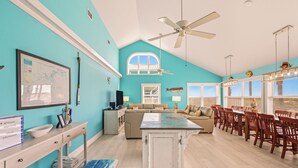 A spacious living area with a large dining table, a ceiling fan, and a view of the outside through a window.