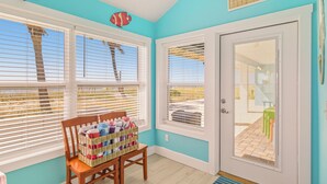 A room with teal walls, a wooden chair with a basket of folded clothes, and a door with a sign reading "Beach House".