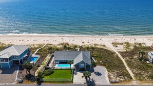 An aerial view of a beachfront property with a swimming pool, a tennis court, and a beach in the background.