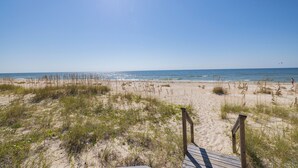 A beach with a wooden boardwalk leading to the water, sandy dunes, and a clear sky.
